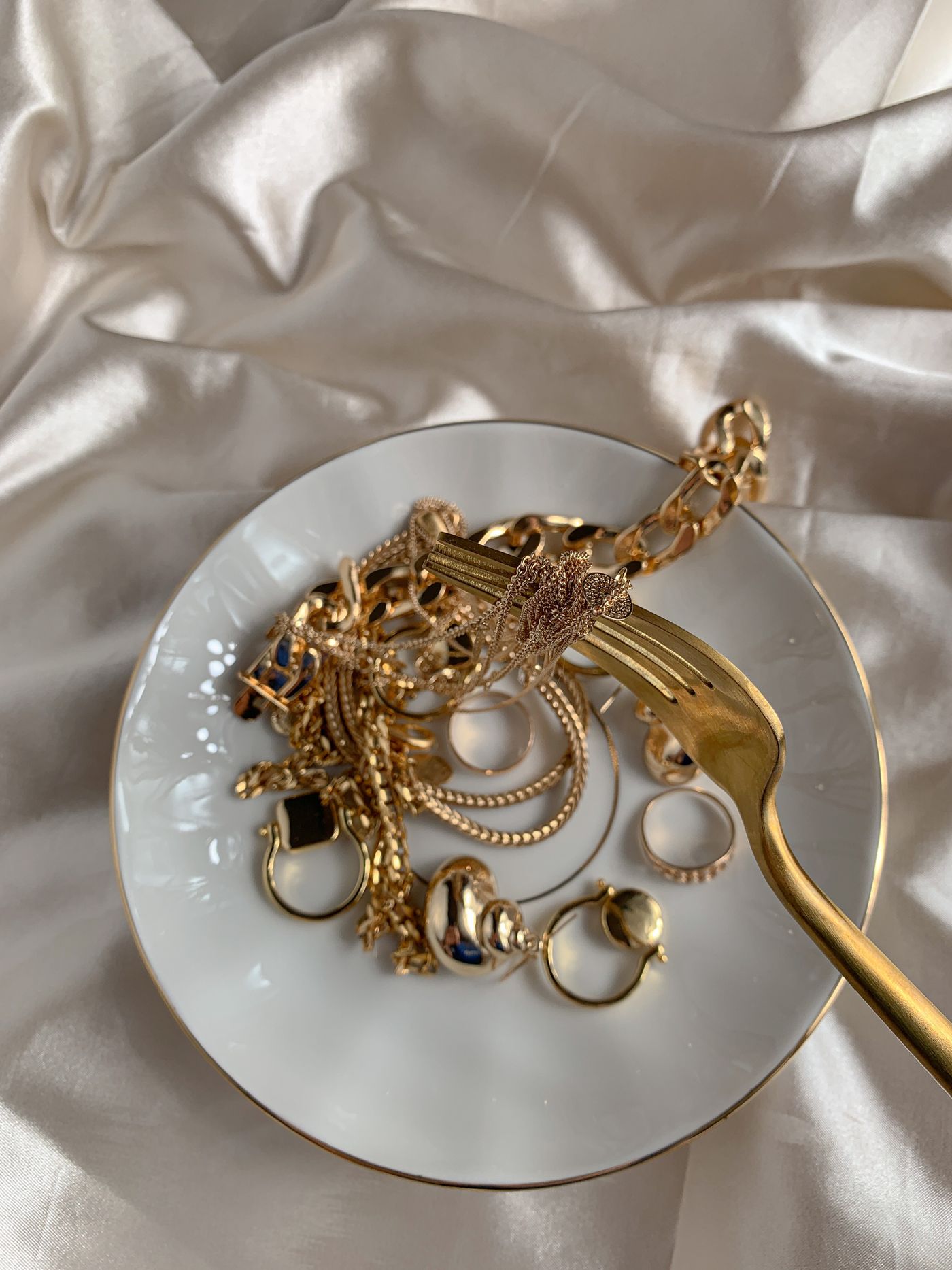 Gold jewellery arranged on a white dish over cream silk